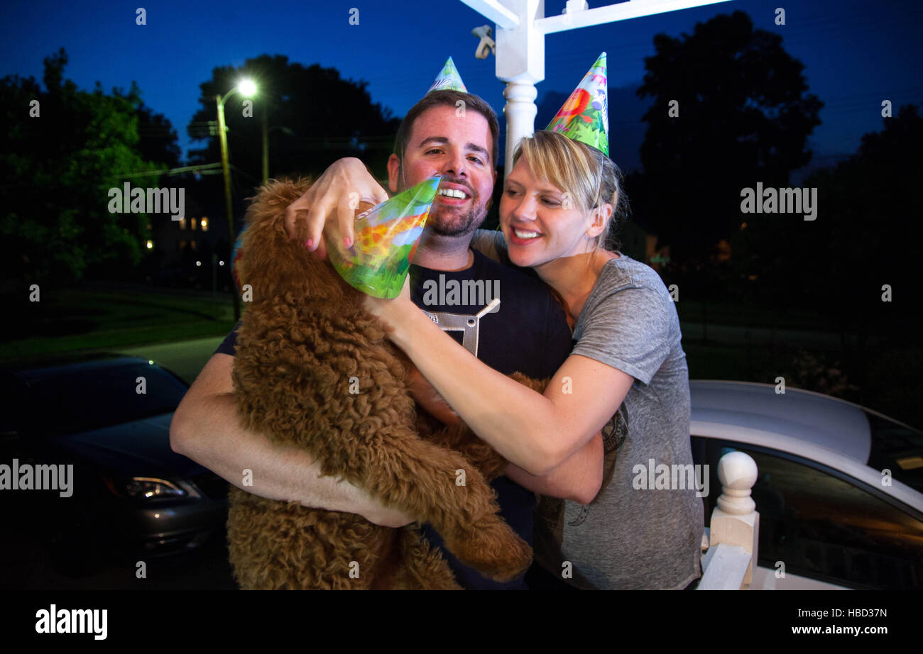 Junges Paar kaukasischen miteinander flirten und Handeln auf einer vorstädtischen Veranda albern halten einen Hund Stockfoto