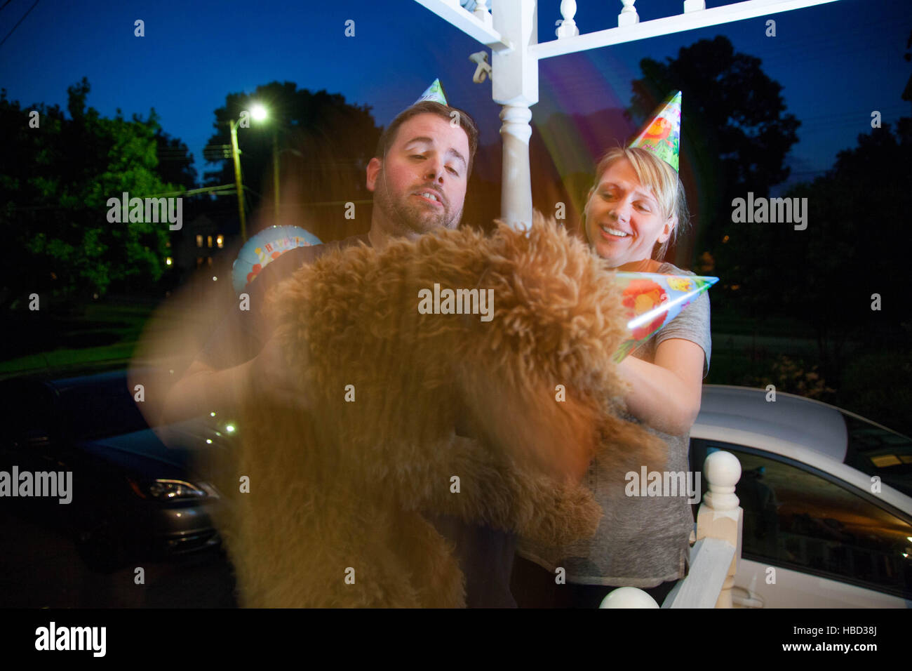 Junges Paar kaukasischen miteinander flirten und Handeln auf einer vorstädtischen Veranda albern halten einen Hund Stockfoto
