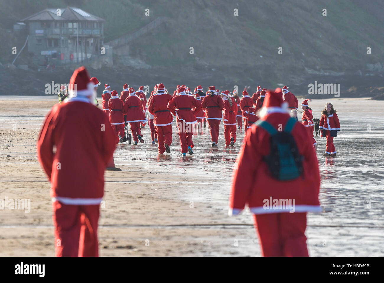 Hunderte von Santas erweisen sich für eine Spendenaktion Volkslauf über eine kühle Fistral Beach in die jährliche Santa Run auf Fistral Beach in Newquay, Cornwall. Stockfoto