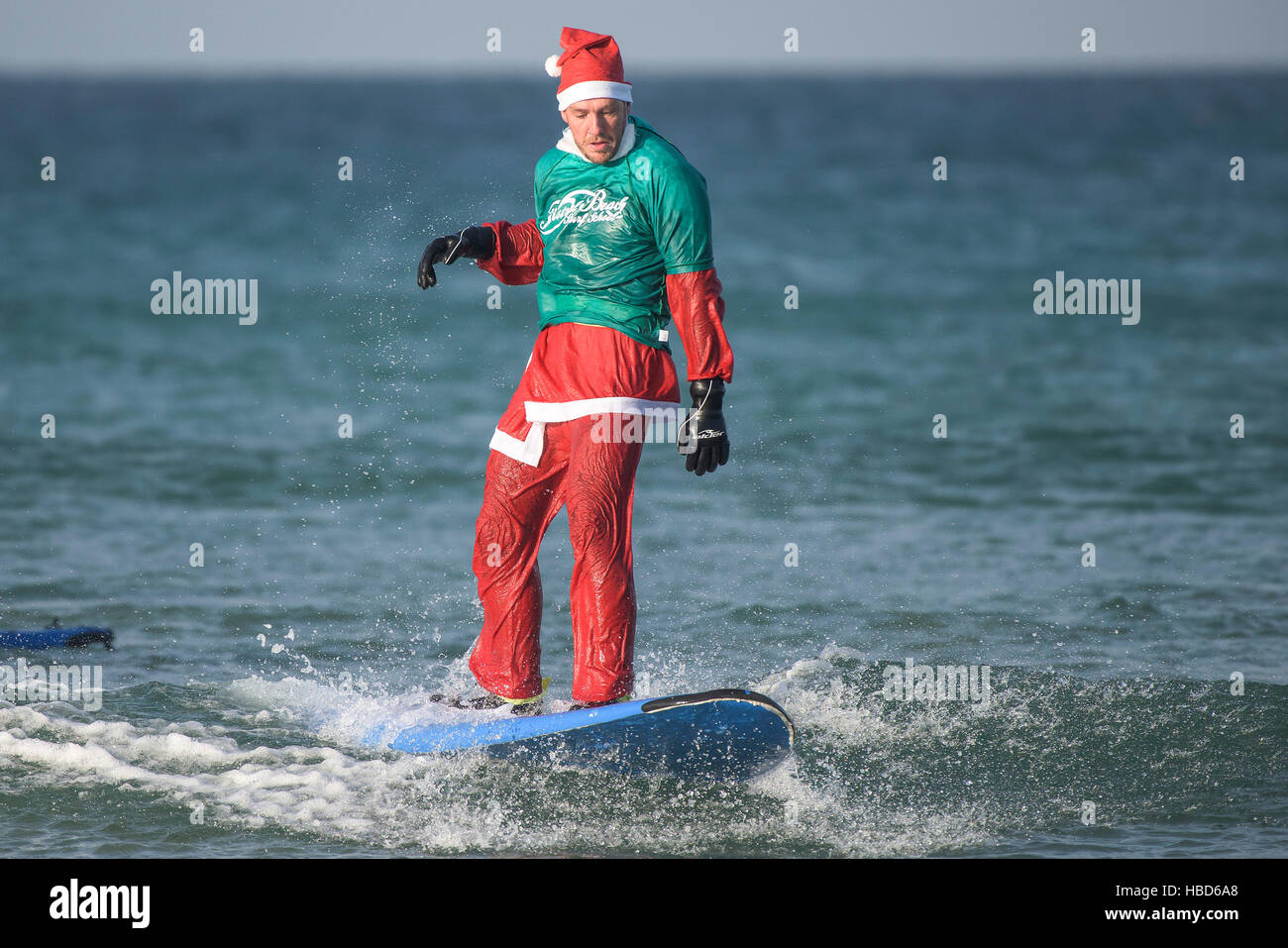 Eine Surf Santa Teilnahme an der jährlichen Geldbeschaffung Santa Surfen Wettbewerb auf einem sehr kühl Fistral Beach in Newquay, Cornwall. UK. Stockfoto