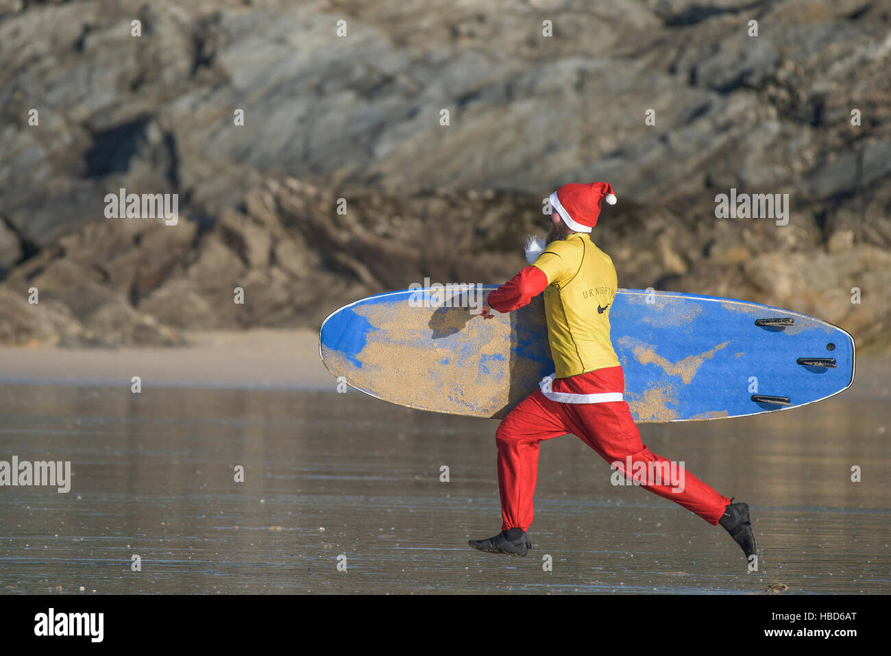 Eine Surf Santa läuft in einem Rennen zu Beginn der Geldbeschaffung Santa Surfen Wettbewerb auf einem sehr kühl Fistral Beach in Newquay, Cornwall. UK. Stockfoto