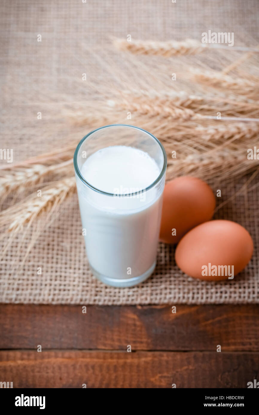 Glas Milch, zwei Eiern mit Hüttenkäse und Ähren auf die Serviette von einer Leinwand auf dem alten Holztisch liegen Stockfoto