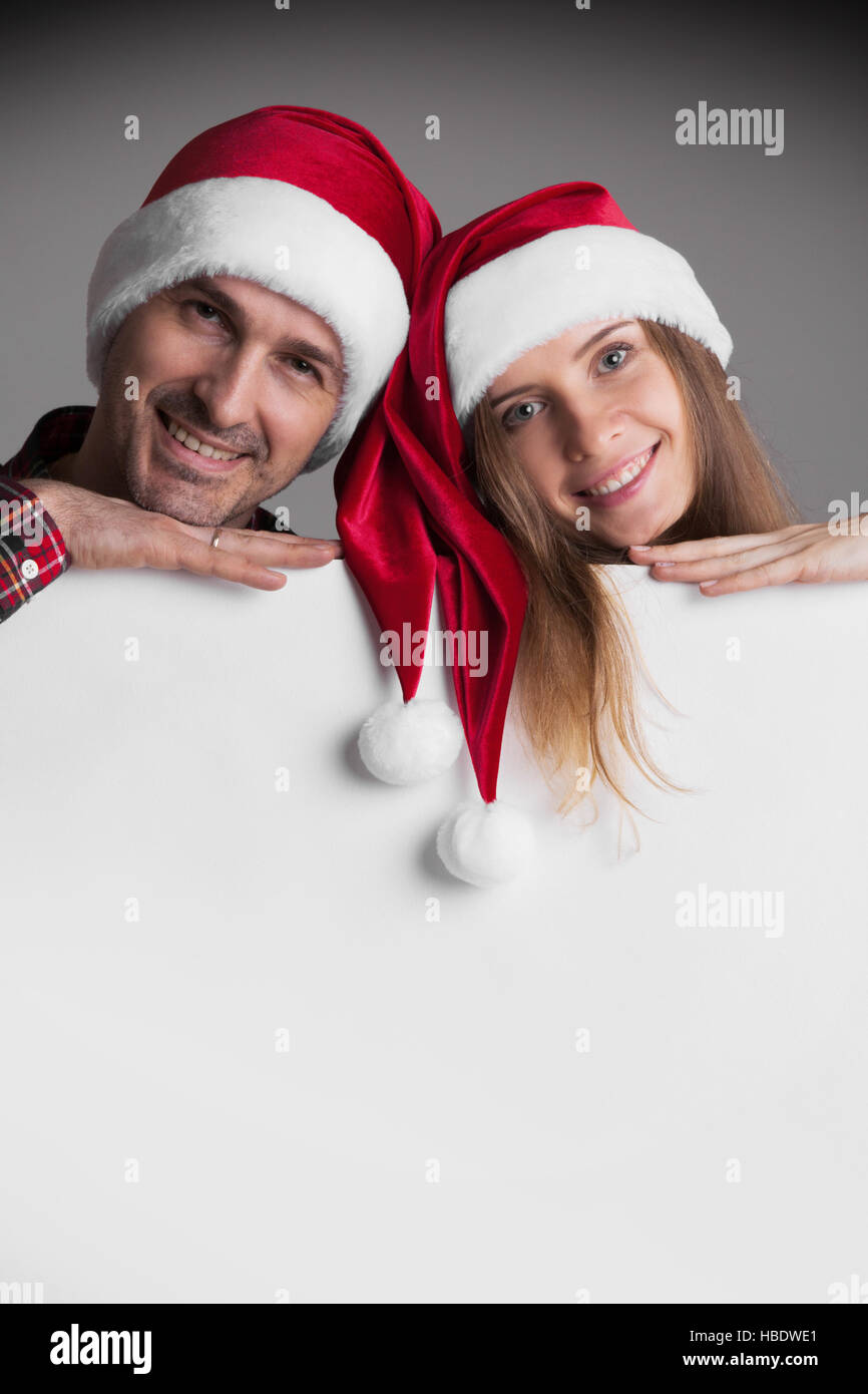 Glücklich lächelnd paar in Santas Hüte mit weißen leeren Banner mit Textfreiraum Stockfoto
