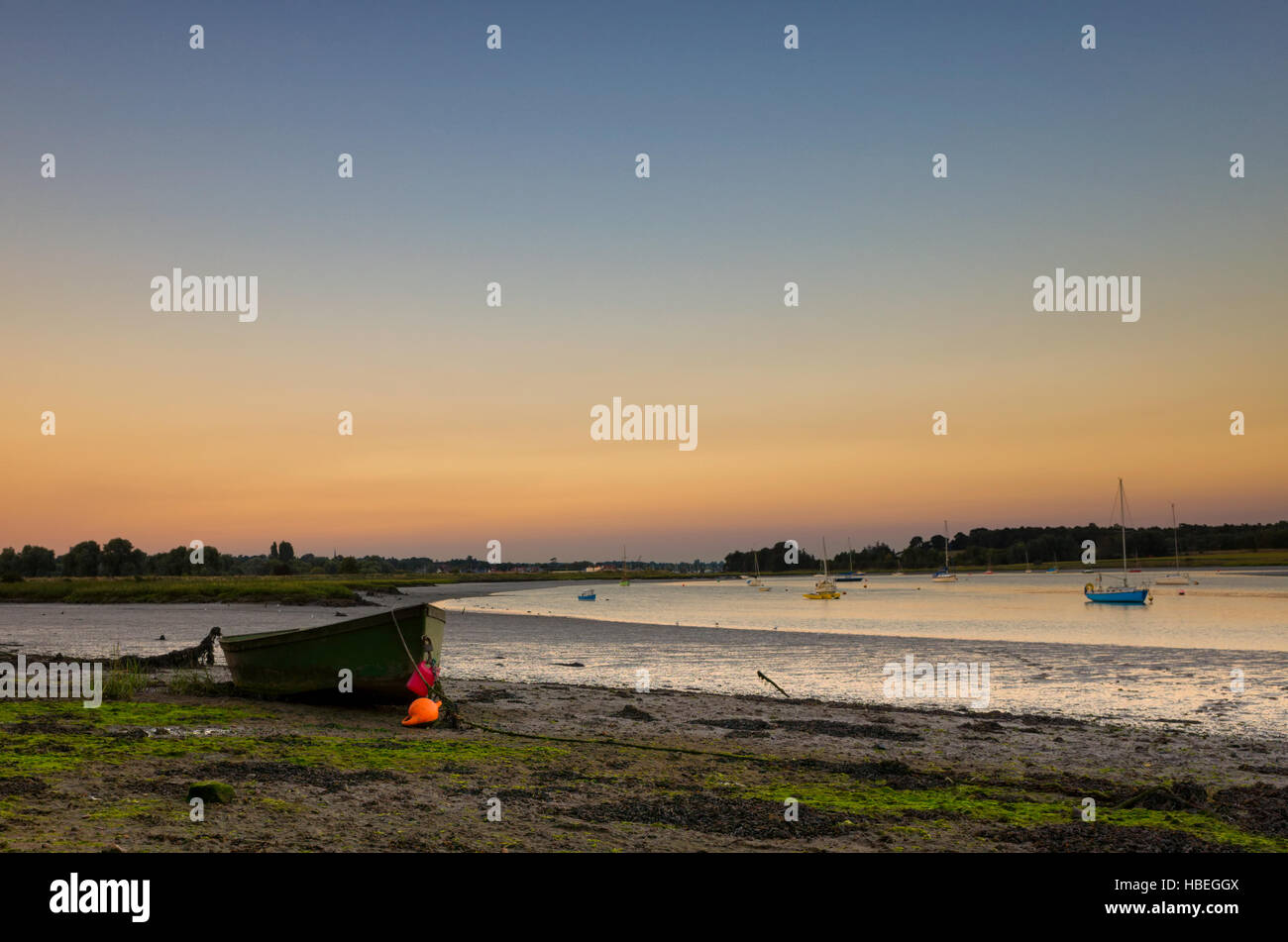 River Deben Woodbridge, England. Ein kleines Boot geerdet am Ufer des Flusses Deben in der Dämmerung. Der Himmel ist blau mit orange knapp über dem Horizont, der auf dem Wasser spiegelt. Dieses Foto wurde kurz nach dem Sonnenuntergang, das macht ein schönes weiches Licht während der frühen Dämmerung genommen. Stockfoto