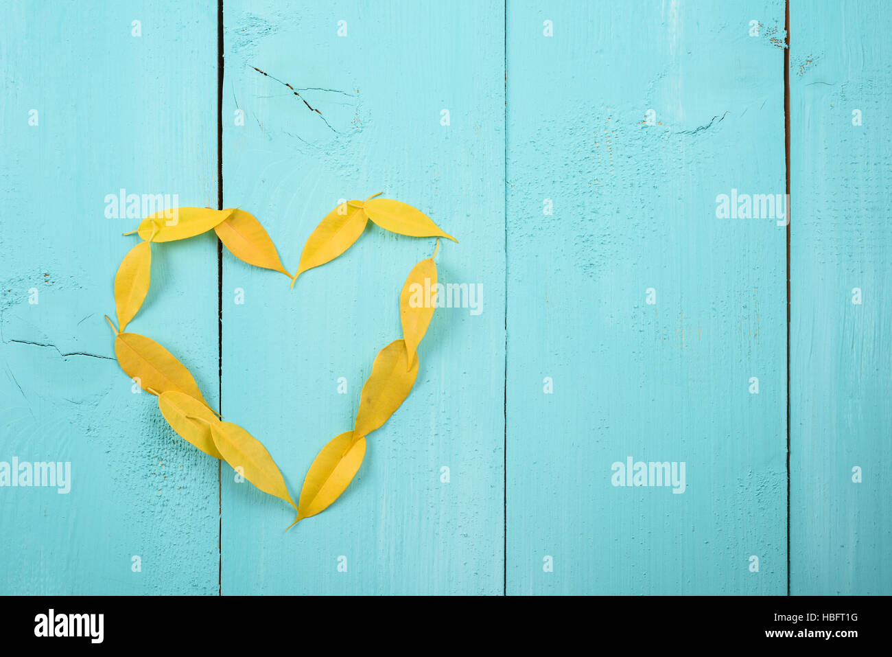 Herzform, die gelbe auf Türkis Holztisch Herbstlaub Stockfoto