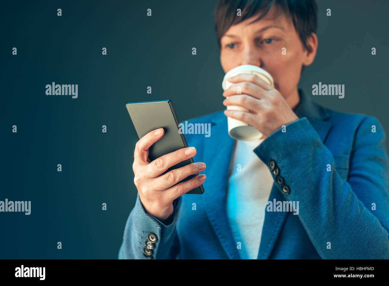 Zufriedene junge Erwachsene Geschäftsfrau Kaffeetrinken zu gehen und mit Blick auf das Handy Stockfoto