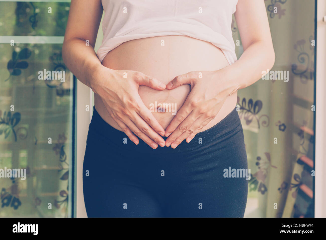 Schwangere Frau hält Hand Herzform für Baby in ihrem Bauch Stockfoto