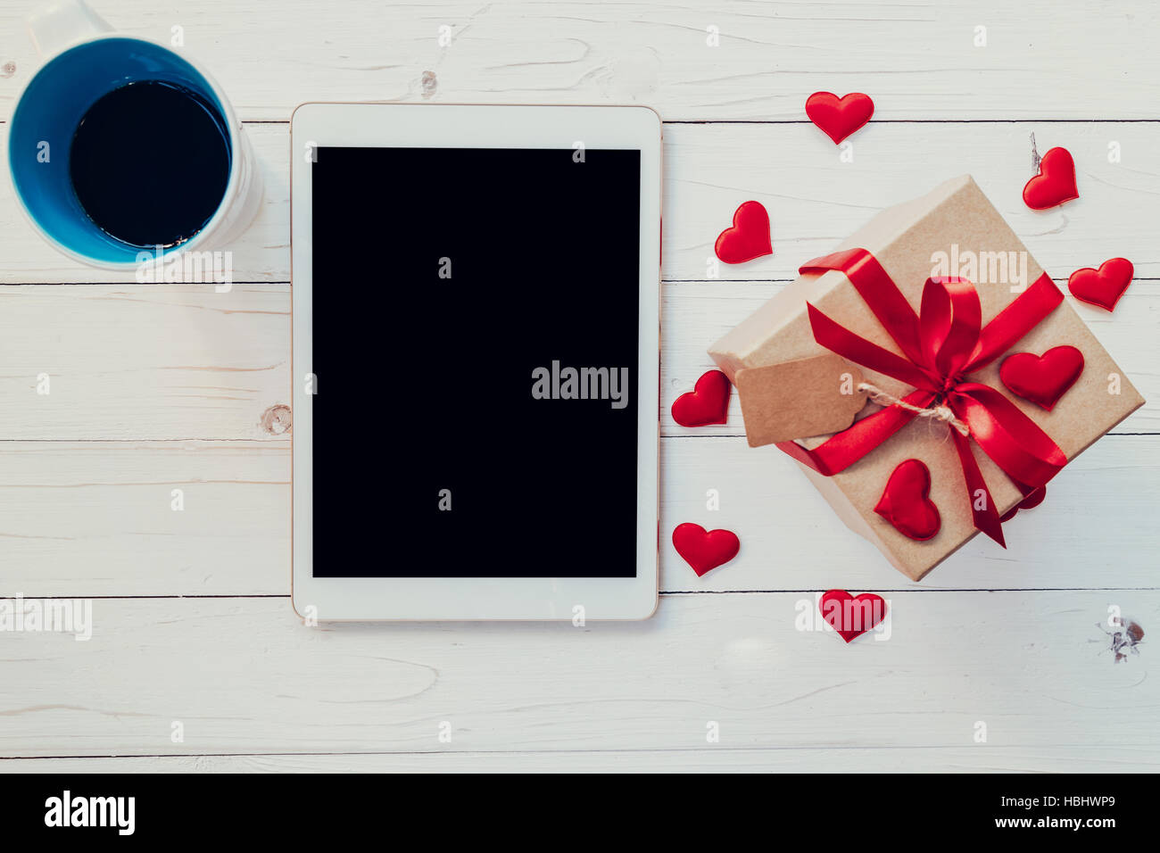 Draufsicht (oben) Geschenk-Box und rotes Band und rotes Herz mit Kaffee und Tablet zum Valentinstag auf Tisch aus Holz. Valentine Hintergrund. Stockfoto