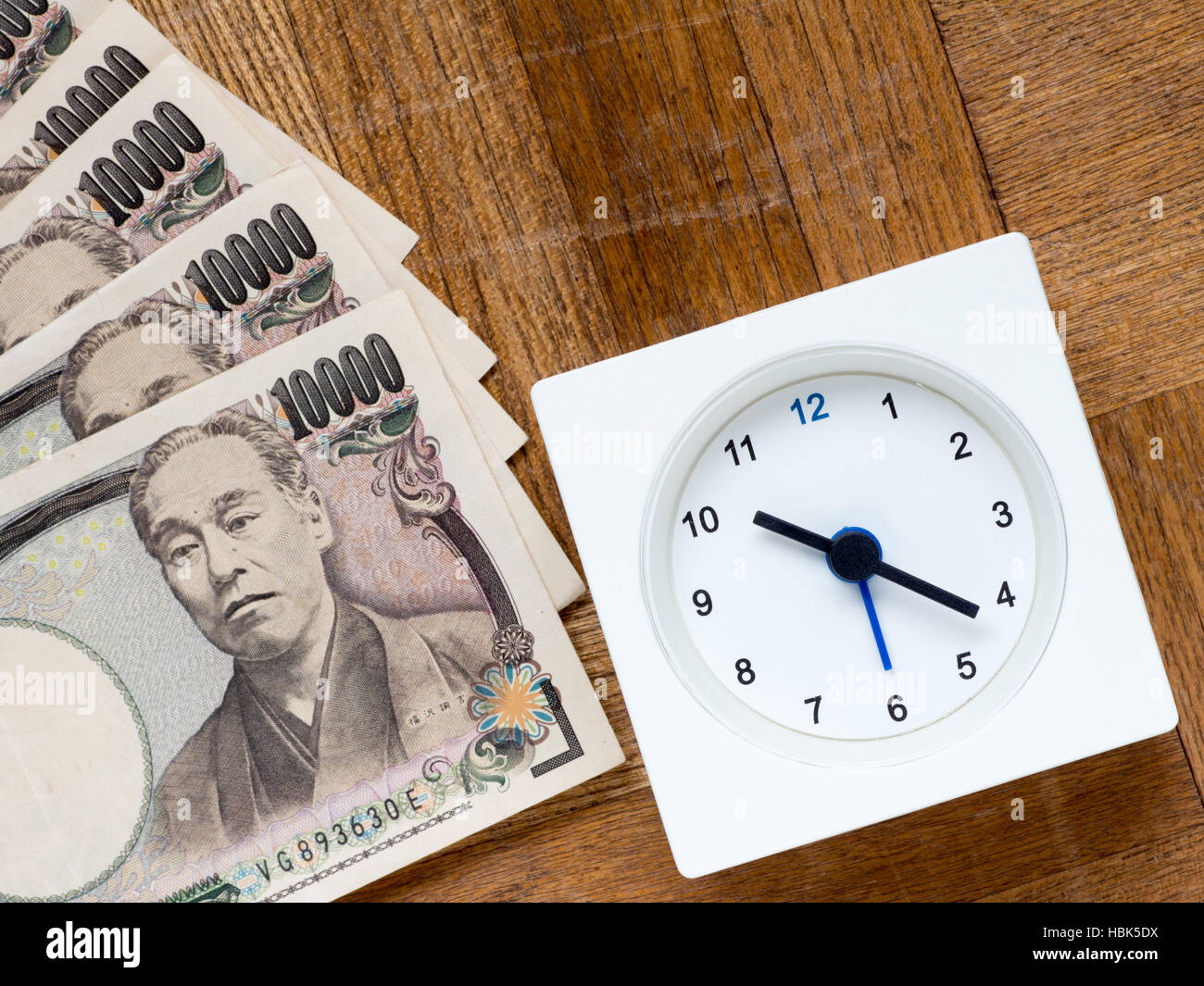 Eine Uhr und japanischen 10000 yen Rechnungen auf die hölzerne Tabelle, die zeigt Zeit ist Geld Stockfoto