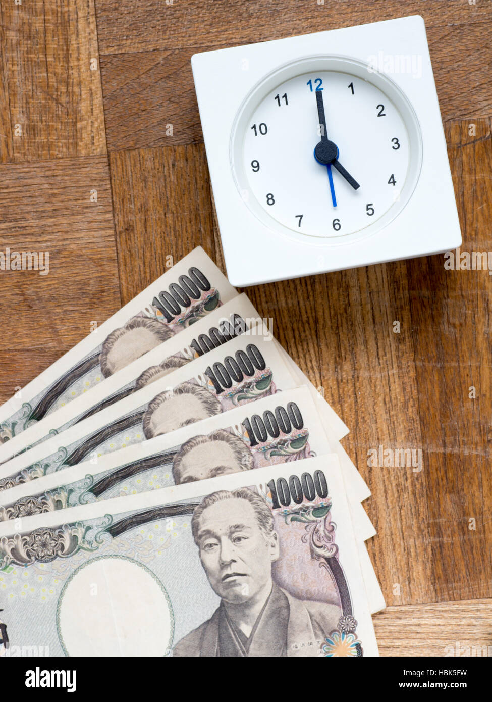 Eine Uhr und japanischen 10000 yen Rechnungen auf die hölzerne Tabelle, die zeigt Zeit ist Geld Stockfoto