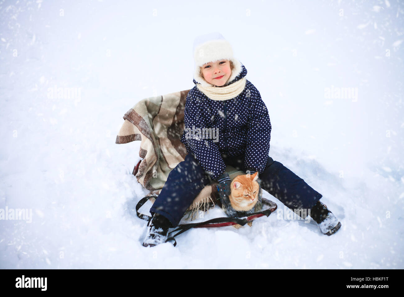 Kleine Mädchen und eine rote Katze auf einem Schlitten fahren in der Landschaft. Stockfoto
