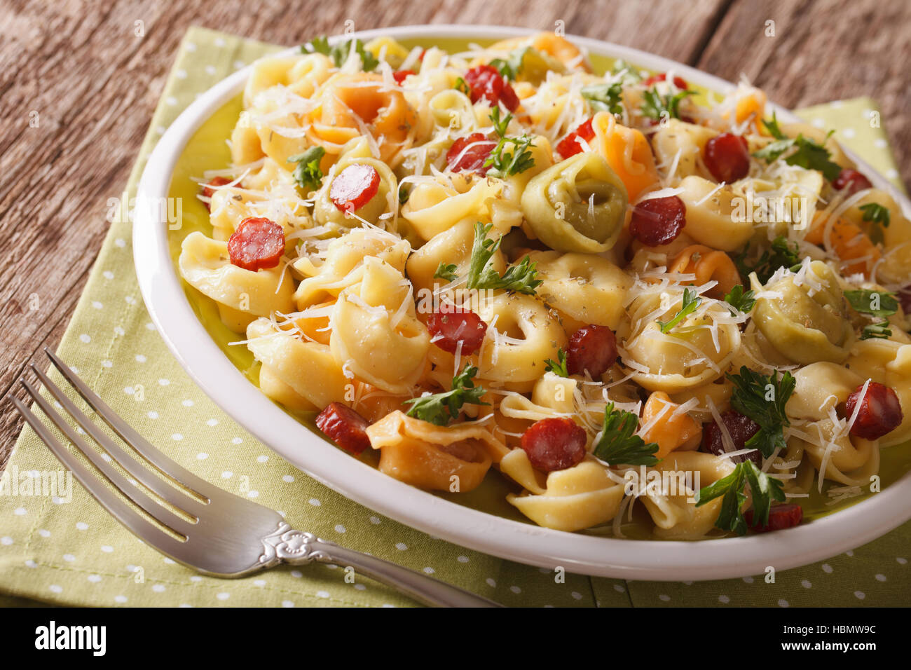 Italienisch gefärbt Tortellini mit Parmesan und in Scheiben geschnittene Wurst Nahaufnahme auf einer Platte. Horizontale Stockfoto