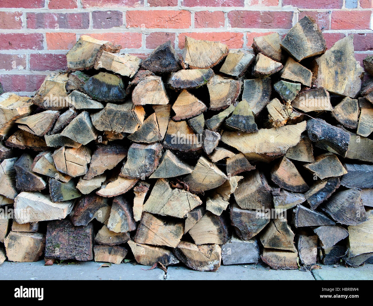 Ein Haufen von Scheitholz gespeichert unter dem Deckmantel einer Wand aus rotem Backstein bereit, auf einem offenen Feuer oder Log Holzofen gebrannt werden. Stockfoto