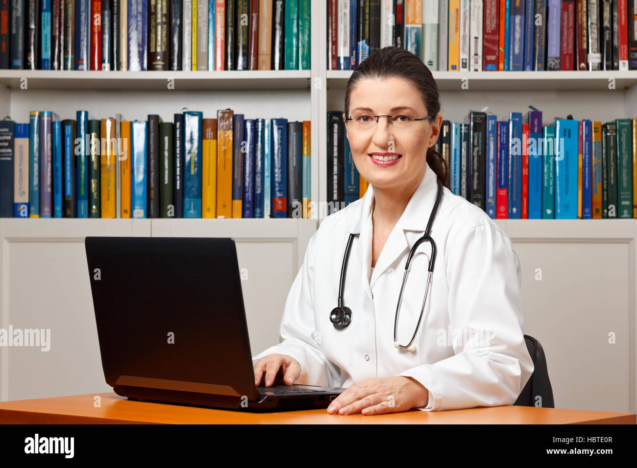 Im mittleren Alter oder Reife weibliche Arzt sitzen an Ihrem Schreibtisch vor einem Computer und lächelt freundlich Stockfoto