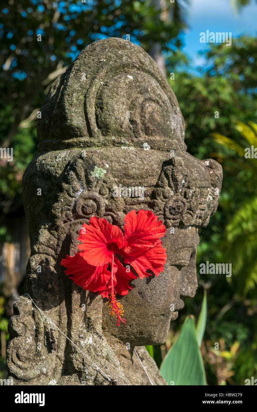 Balinesische Skulptur mit roten Blumen im Garten in Ubud, Bali. Indonesien Stockfoto