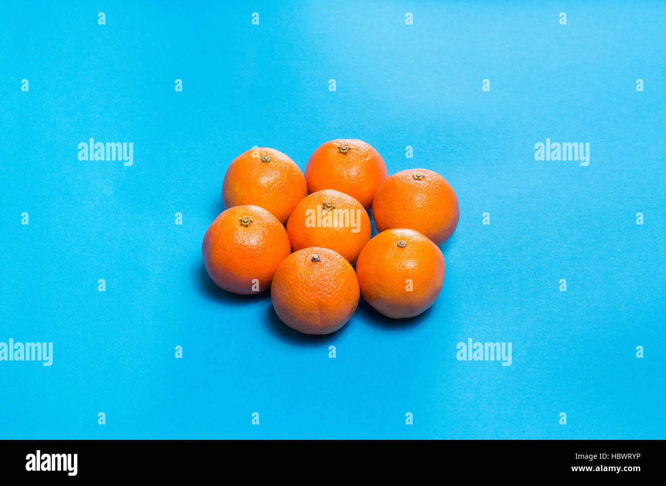 Sonnensymbol aus sechs bunte frische Orangen Mandarinen angelegt auf blaue Tabelle oben gesehen mit Textfreiraum Stockfoto