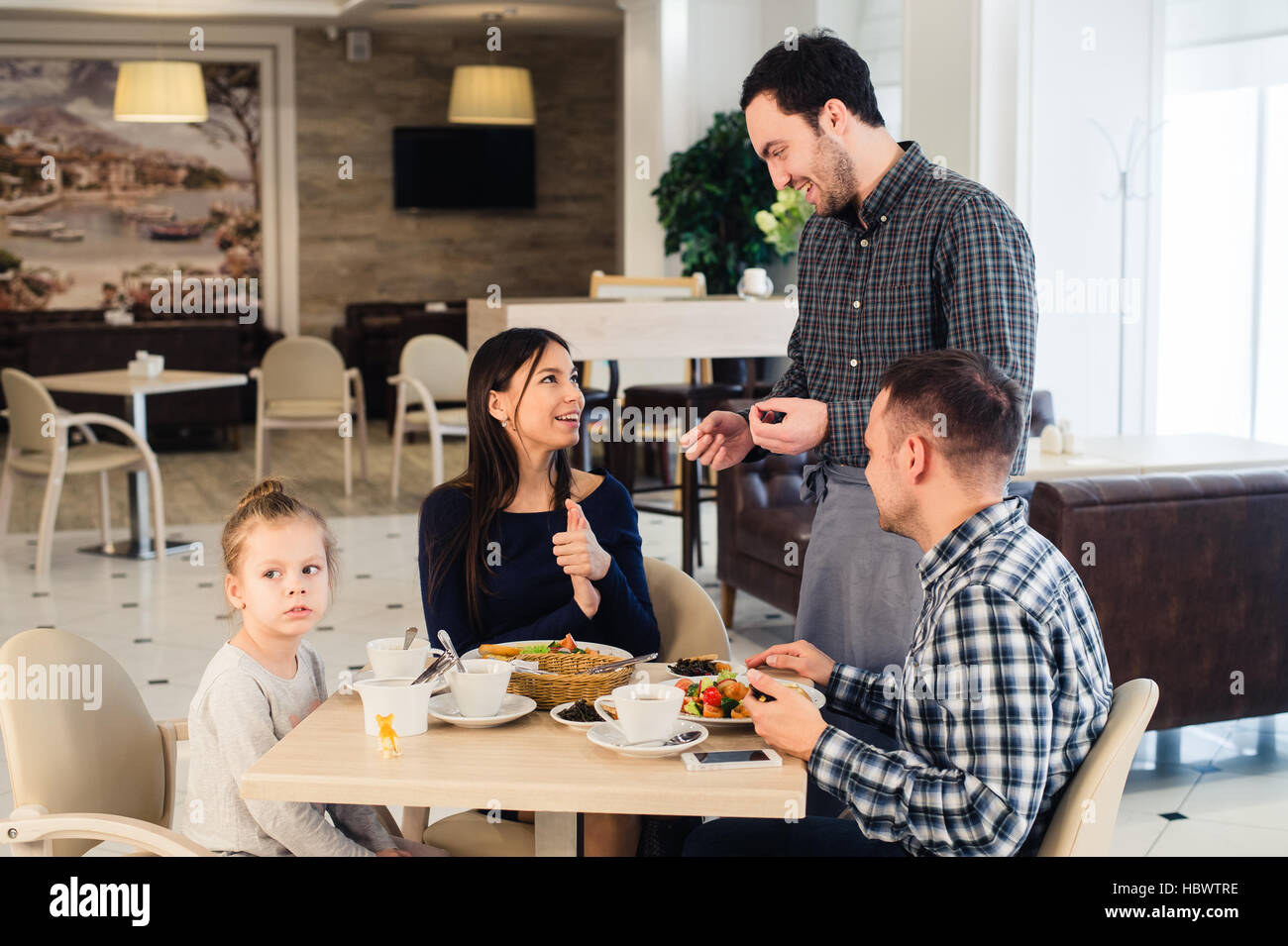 Freundlich lächelnden Kellner die Bestellung am Tisch der Familie beim Abendessen zusammen Stockfoto