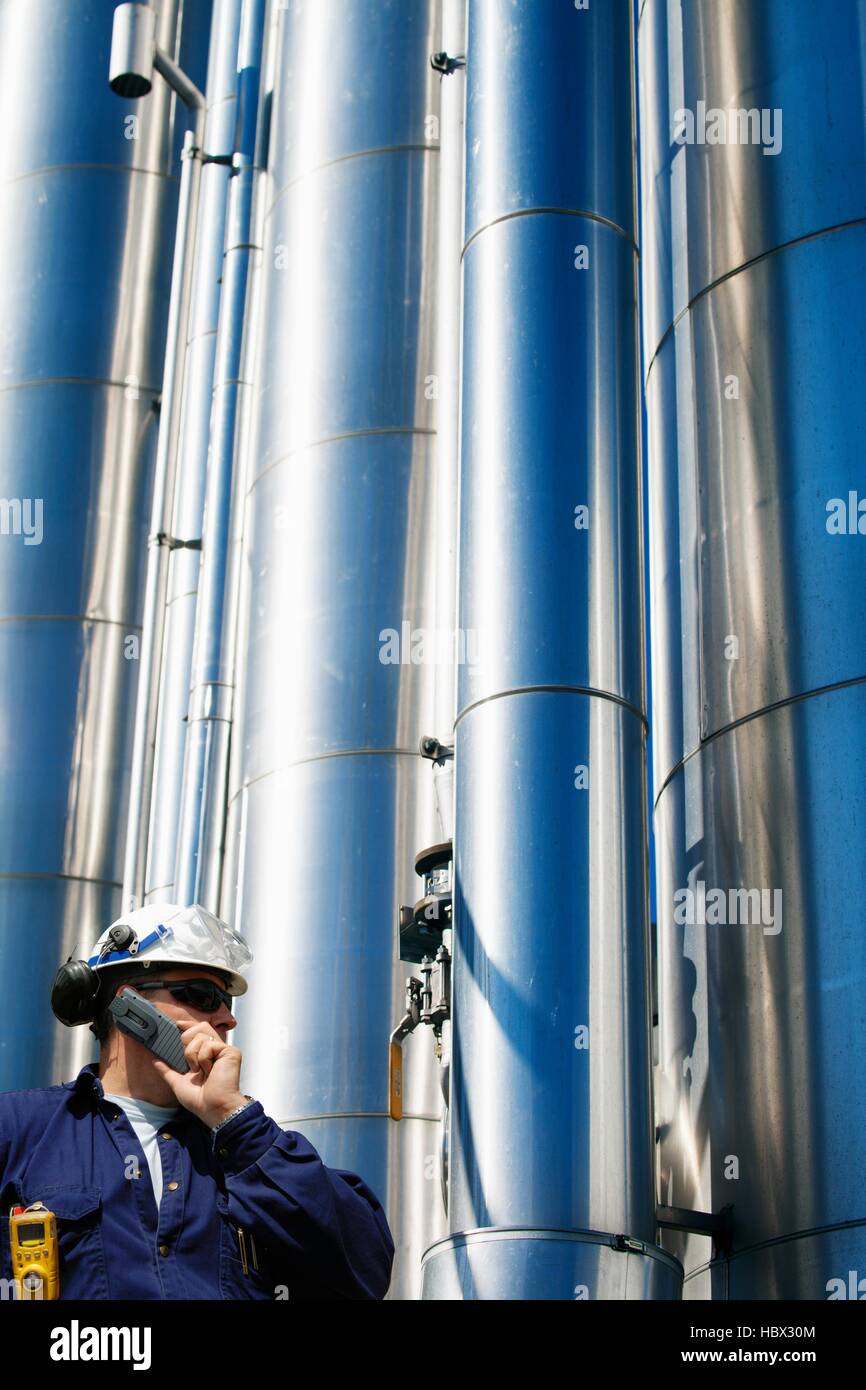 -MODELL VERÖFFENTLICHT. Öl und Gas Arbeiter auf Handy mit Rohren im Hintergrund. Stockfoto