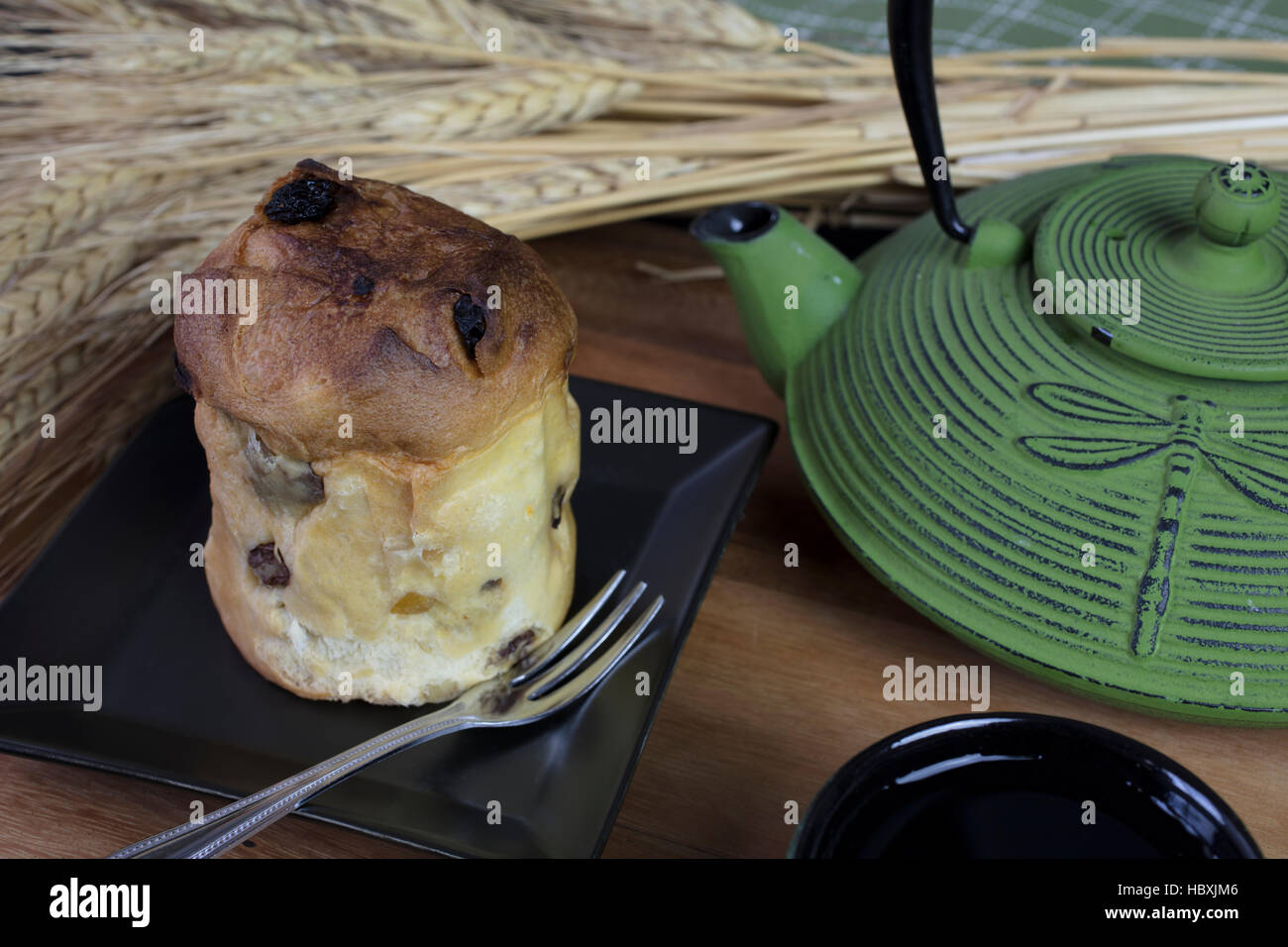 Miniatur-Panettone-Brot auf einem schwarzen quadratischen Teller serviert, begleitet von einem Topf von grünem Tee Stockfoto