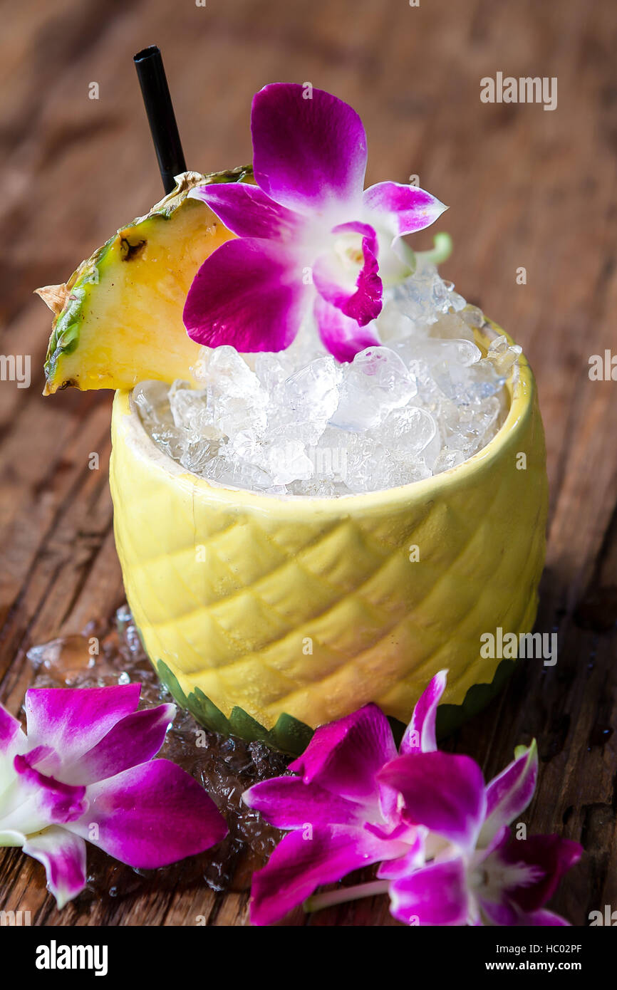 Tiki cocktail in einer Ananas-Becher mit frischer Ananas und Orchidee Blume Beilagen serviert. Stockfoto