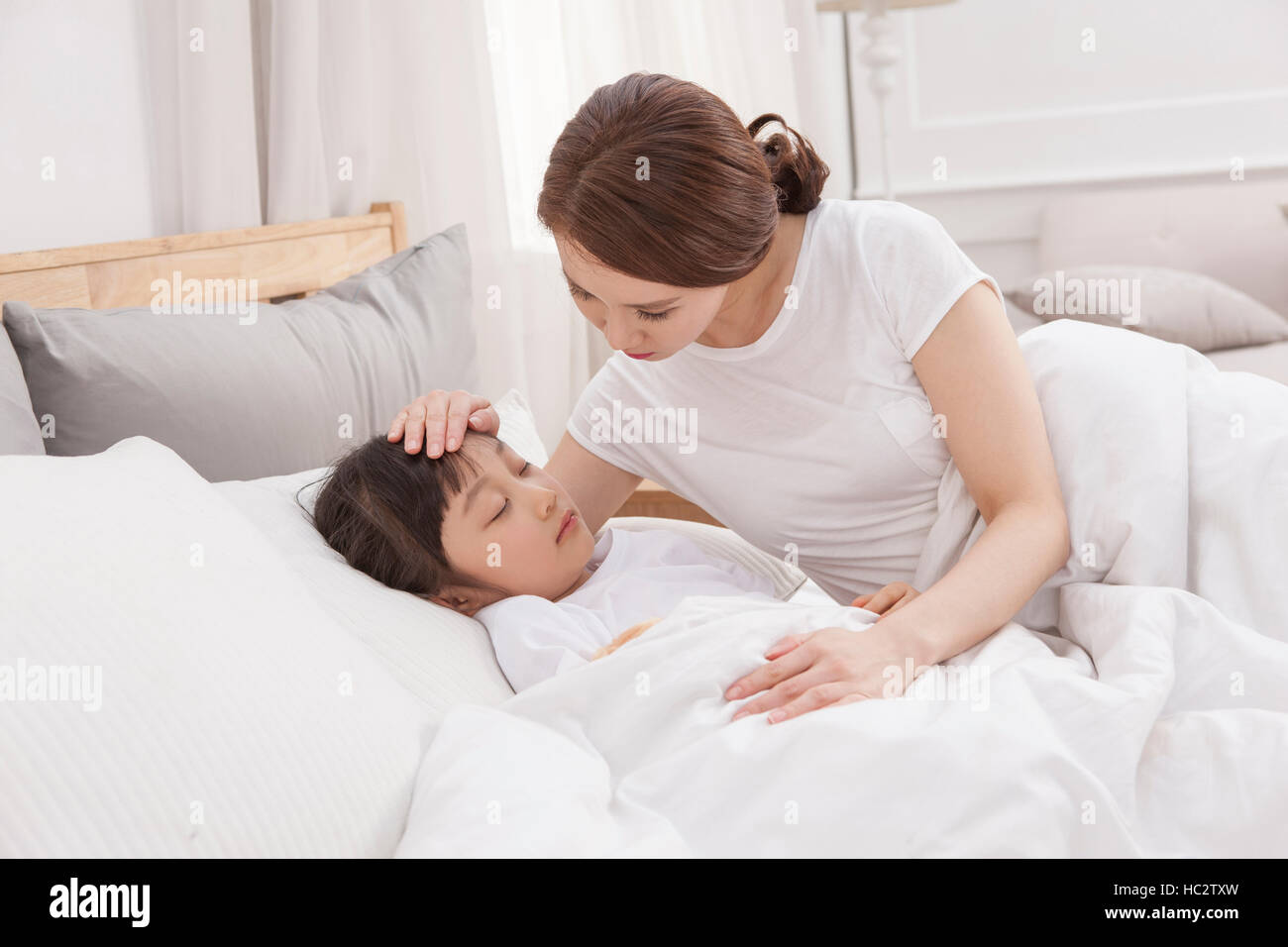 Liebevolle Mutter setzen ihre Tochter im Bett zu schlafen Stockfoto