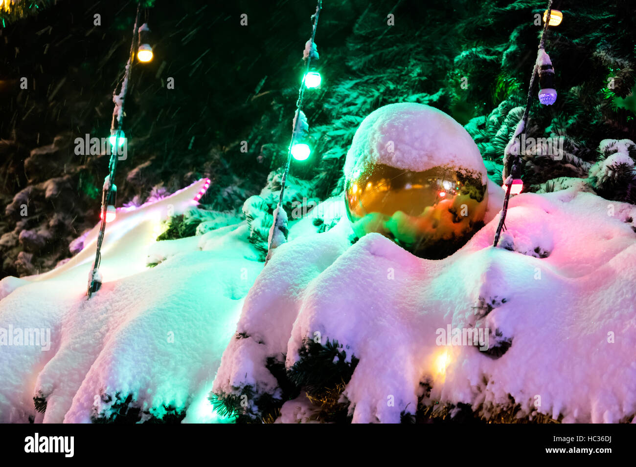 große Weihnachts-Ball mit Schnee oben auf schneebedeckten Tanne Äste unter bunten Weihnachtsbeleuchtung Stockfoto