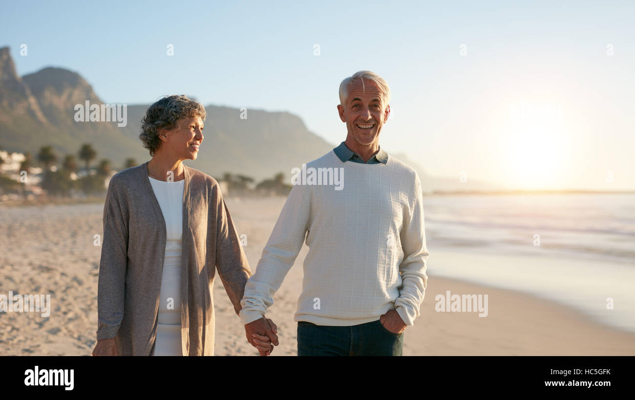 Im Freien Schuss glücklich älteres paar spazieren am Strand. Senior Mann und ältere Frau bei einem Spaziergang am Ufer Meeres. Stockfoto