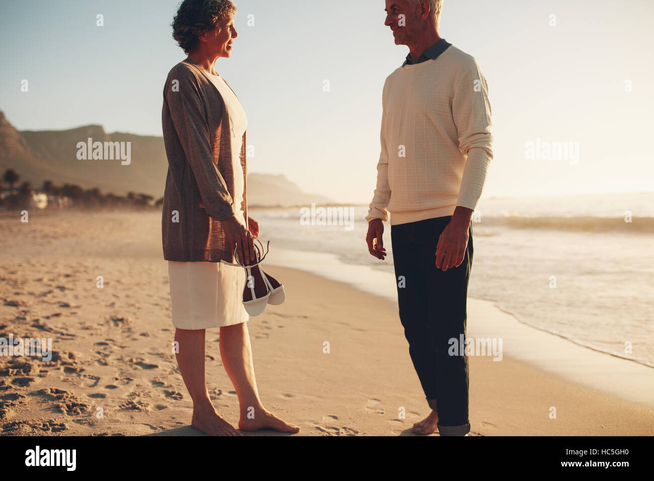 Im Freien Schuss glücklich älteres paar stehen am Strand zusammen und reden. Senior Mann und ältere Frau am Ufer Meeres. Stockfoto