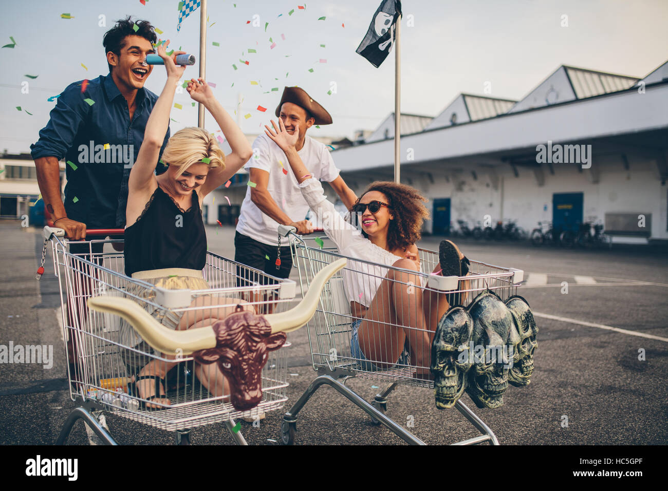 Multiethnische Jugendlichen racing mit Warenkorb. Junge Freunde, die Spaß an einem shopping Carts und Konfetti. Stockfoto