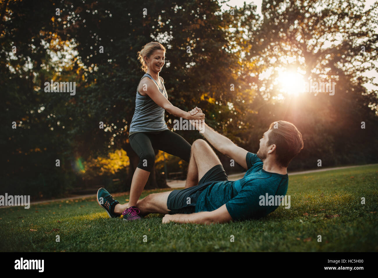 Aufnahme der jungen Frau, die Menschen vom Boden aufstehen helfen. Gesunde junge Paar im Park trainieren zusammen. Stockfoto