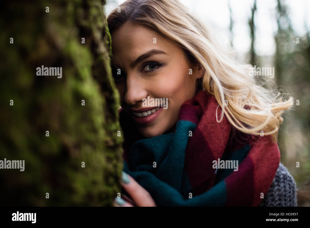 Schöne Frau versteckt sich hinter Baumstamm im Wald Stockfoto