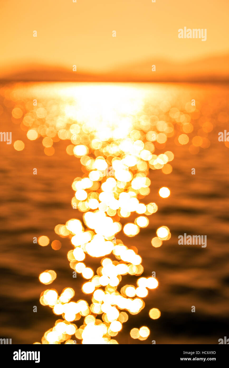 Verschwommenes Bild der schönen Sonne Reflexion über Meereswellen bei Sonnenuntergang, absichtlich Out of Focus für Nutzung im Hintergrund... Stockfoto