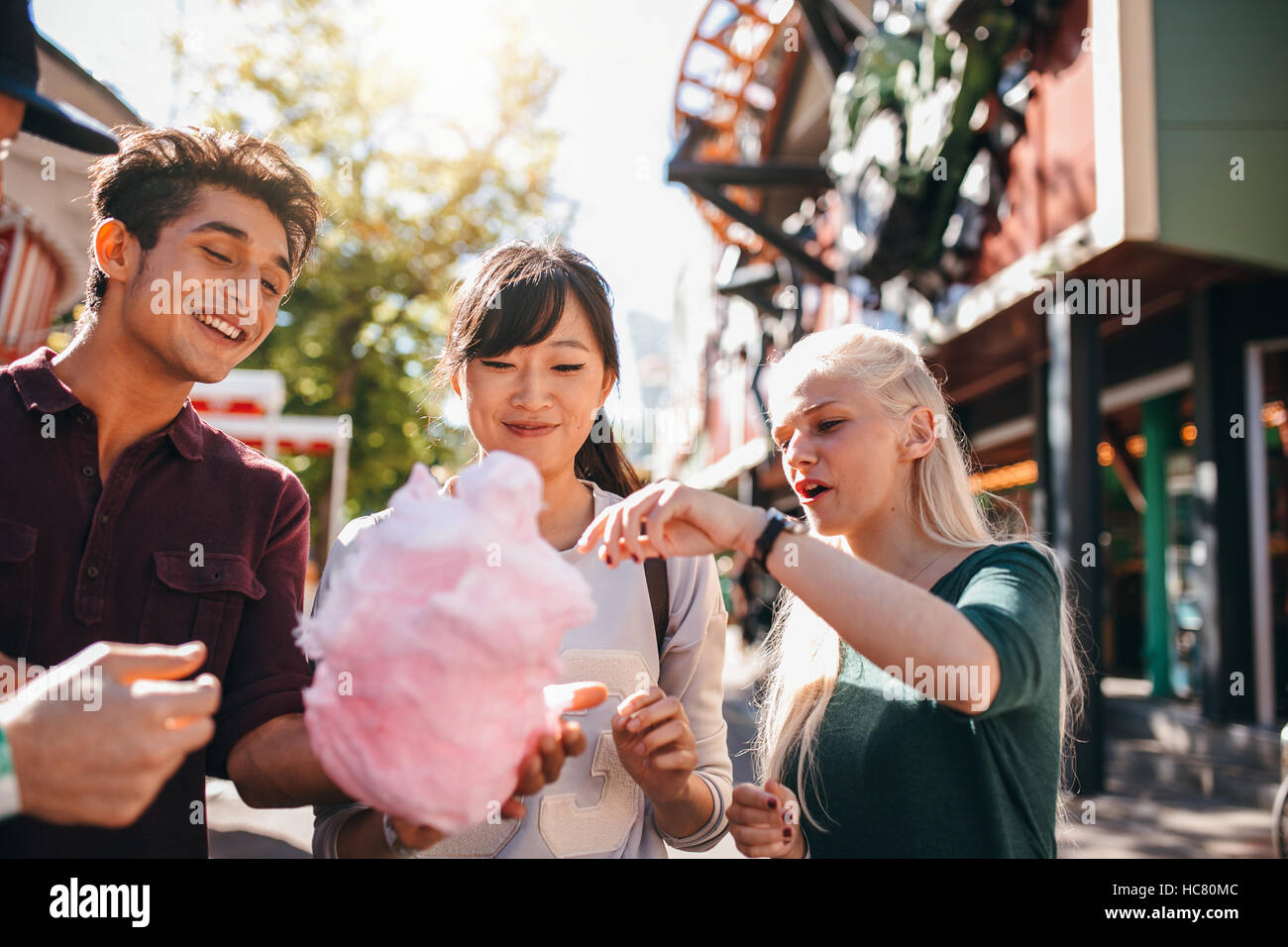 Gruppe von Freunden essen Zuckerwatte im Vergnügungspark. Junge Männer und Frauen teilen Baumwolle Zuckerwatte an Karneval. Stockfoto