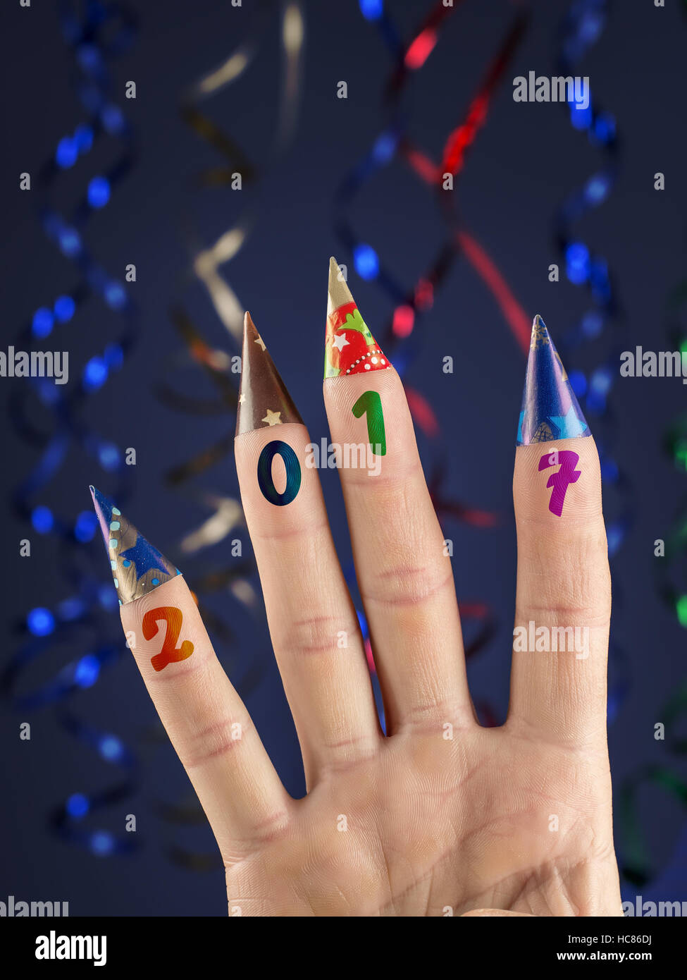 Vier Finger mit aufgedruckten Datum 2017 mit Papiertütchen auf dunkelblauem Hintergrund mit Luftschlangen geschmückt Stockfoto