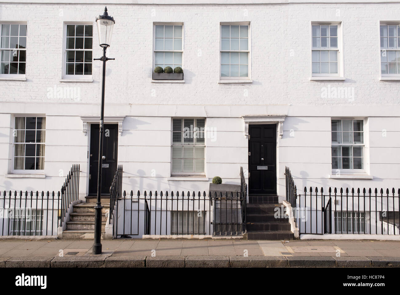 Fassade eines britischen viktorianischen weißen Wohngebäude mit schwarzen Türen und Metallzaun. Bürgersteig und Straße Lampe davor. Stockfoto