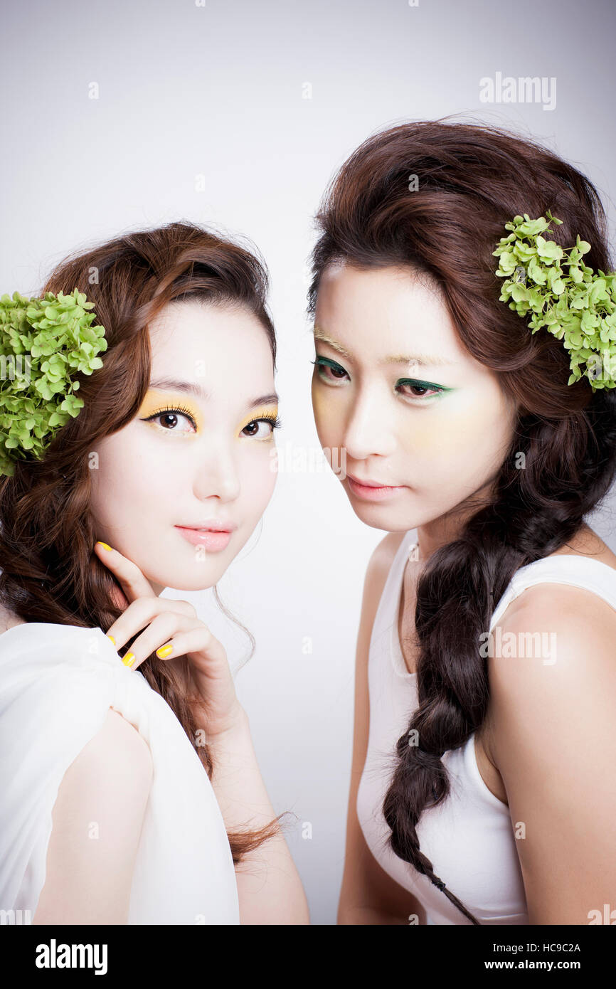 Porträt von zwei junge Koreanerinnen mit grünen Blumen auf ihre lange gewellte Haar posiert Stockfoto