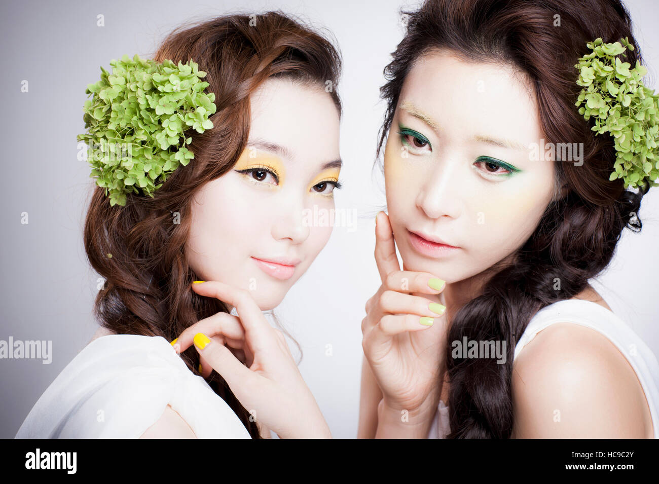 Porträt von zwei junge Koreanerinnen mit grünen Blumen auf ihre lange gewellte Haar posiert Stockfoto