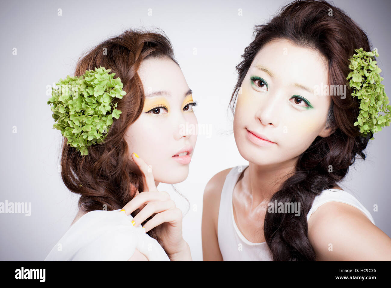 Porträt von zwei junge Koreanerinnen mit grünen Blumen auf ihre lange gewellte Haare Stockfoto