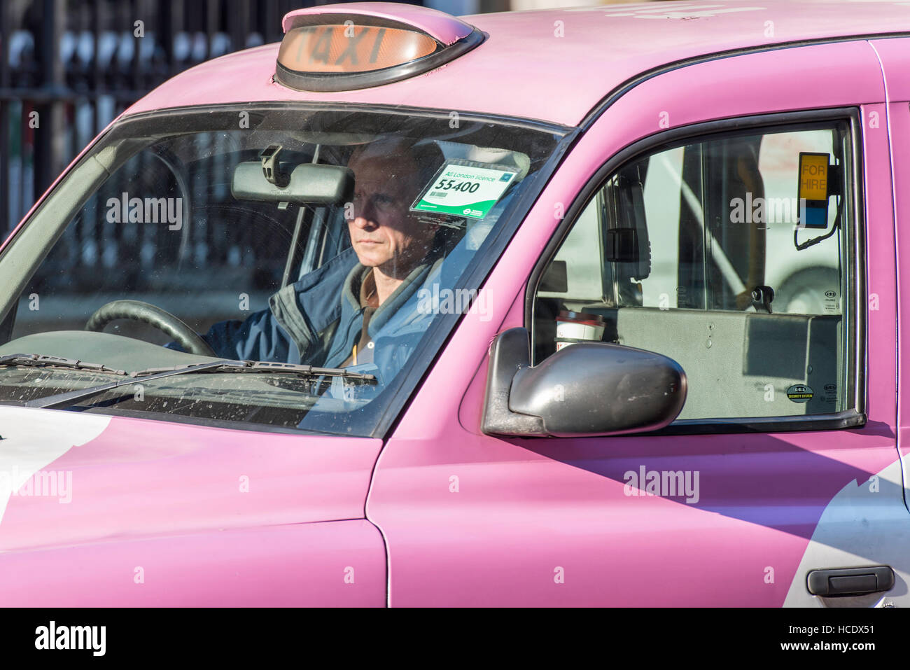 Ein Reifen männlichen Taxifahrer im Verkehr in seinem rosa Taxi sitzen. Die Zeichen liest gemietet "so er für Passagiere zu Hagel ihn für eine Reise wartet. Stockfoto