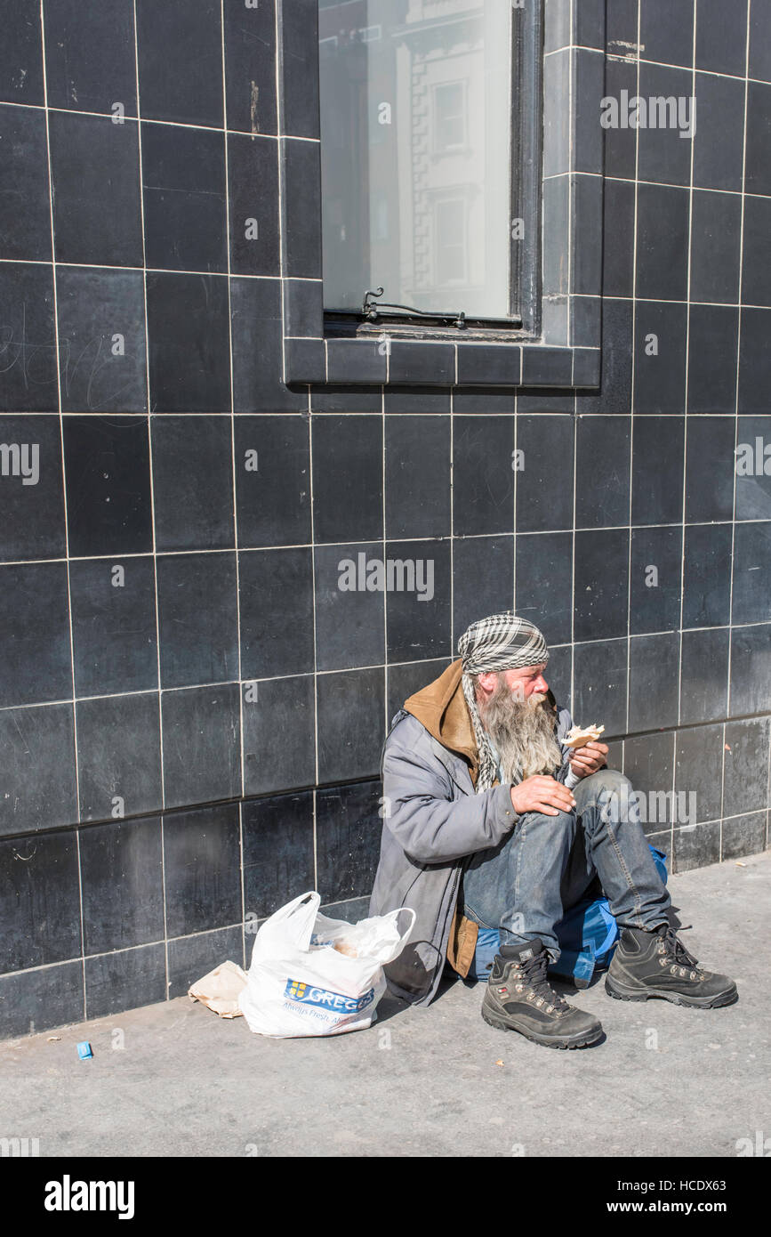 London, England, Vereinigtes Königreich, 21. April 2016. Ein Obdachloser sitzt unter einem Fenster ein Sandwich zu essen. Stockfoto
