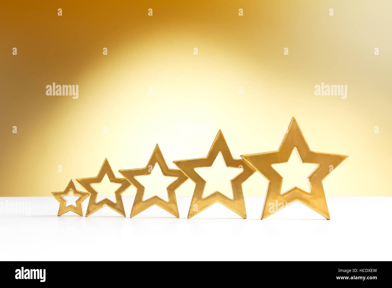 Fünf Goldene strahlende Sterne in aufsteigender Reihenfolge auf weißen und gelben Hintergrund mit einem Scheinwerfer, Textfreiraum Stockfoto
