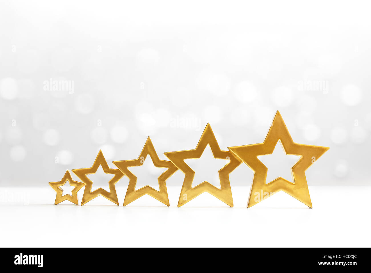 Fünf brillant glänzenden goldenen Sternen in aufsteigender Reihenfolge auf weißem Hintergrund mit funkelnden Lichtern, Textfreiraum Stockfoto