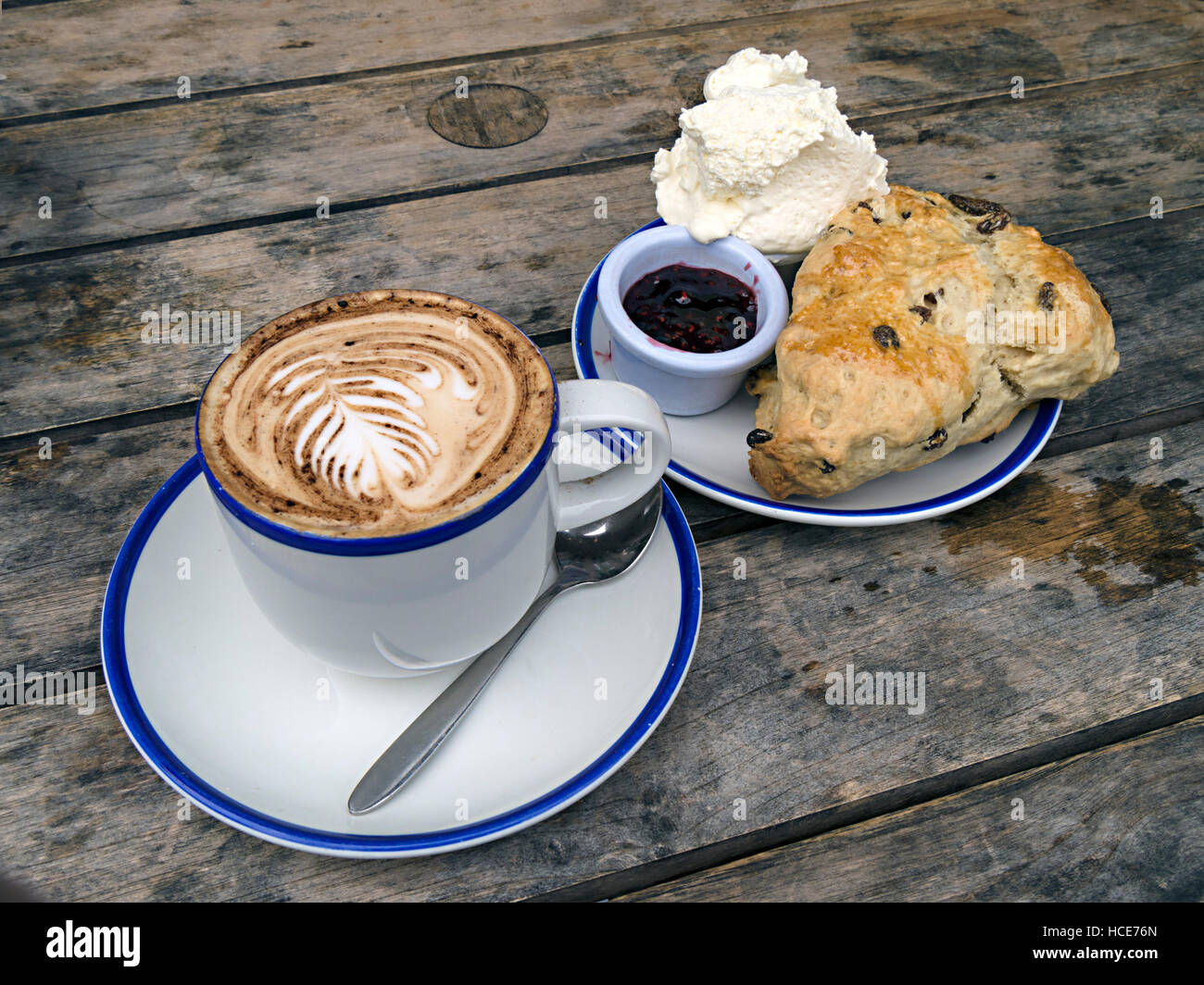 Tasse Cappuccino-Kaffee, Obstscone, Kanne mit Marmelade und Sahne auf einem Tisch mit Holzlatten, Chester's Cafe, Cumbria, England, Großbritannien. Stockfoto