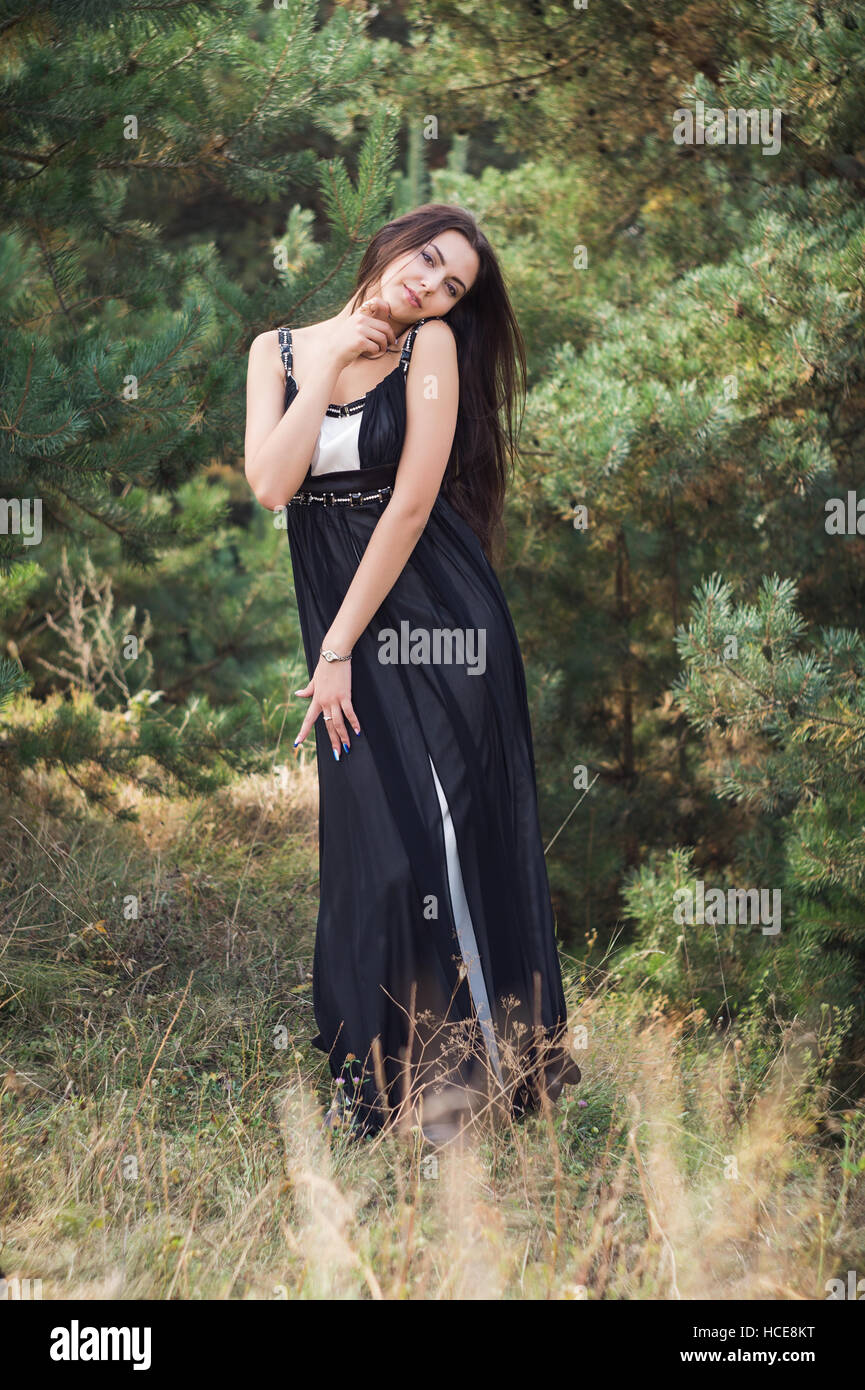 Anmutig bezaubernde Brünette Model posiert im schwarzen Kleid in Nadelwäldern park Stockfoto