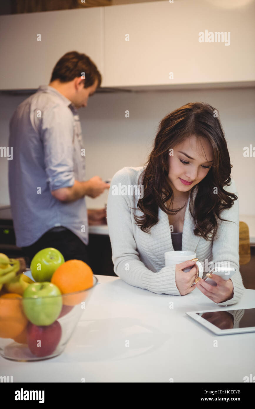 Frau mit Handy während der Mann im Hintergrund arbeitet Stockfoto