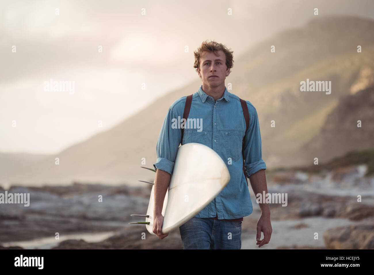 Mann trägt ein Surfbrett zu Fuß auf dem Seeweg Stockfoto