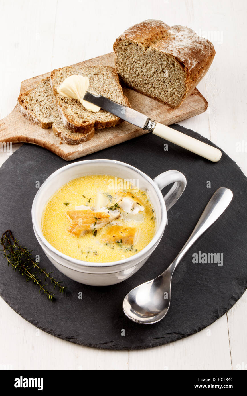 traditionelle schottische Fischsuppe, Cullen Skink, gebacken mit Kartoffeln in einer grauen Ton Tasse auf eine Runde Schiefer und home Soda Brot auf Holzbrett Stockfoto
