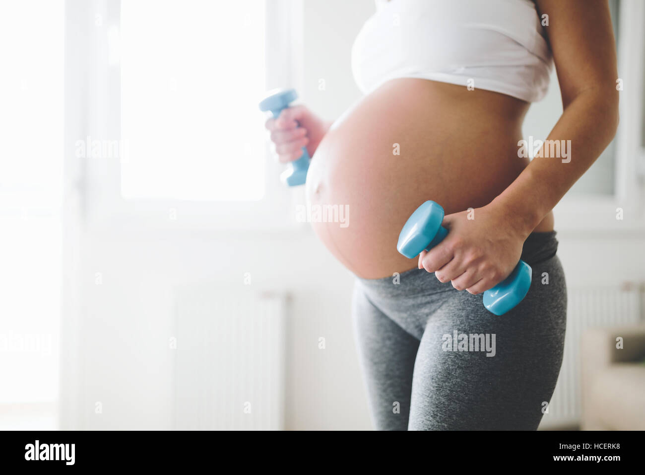 Sportliche schwangere Frau, die das Training mit Hanteln Stockfoto