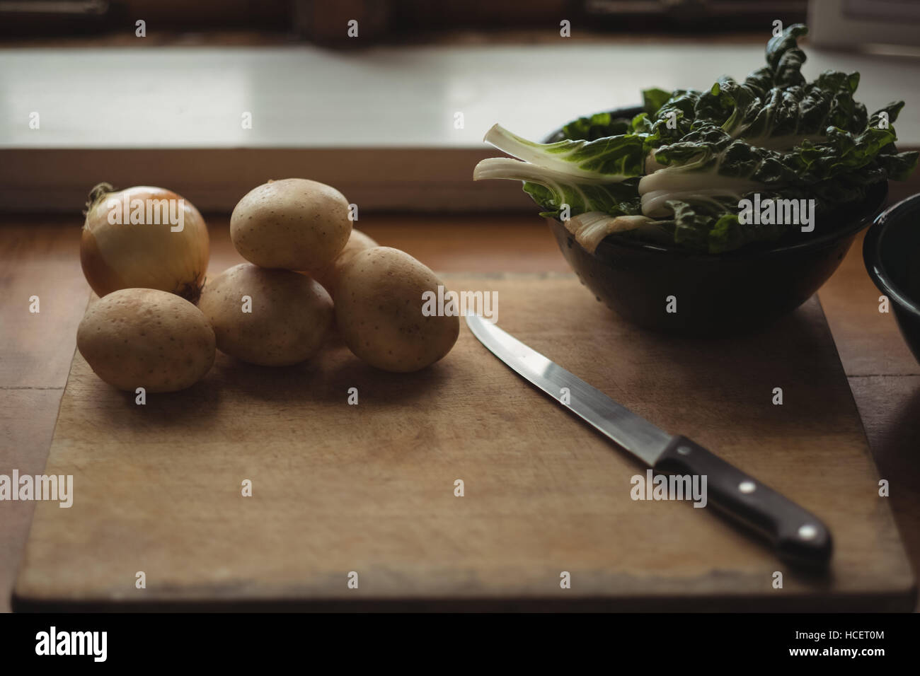 Kartoffeln, Zwiebeln und Salat auf Schneidebrett mit Messer Stockfoto
