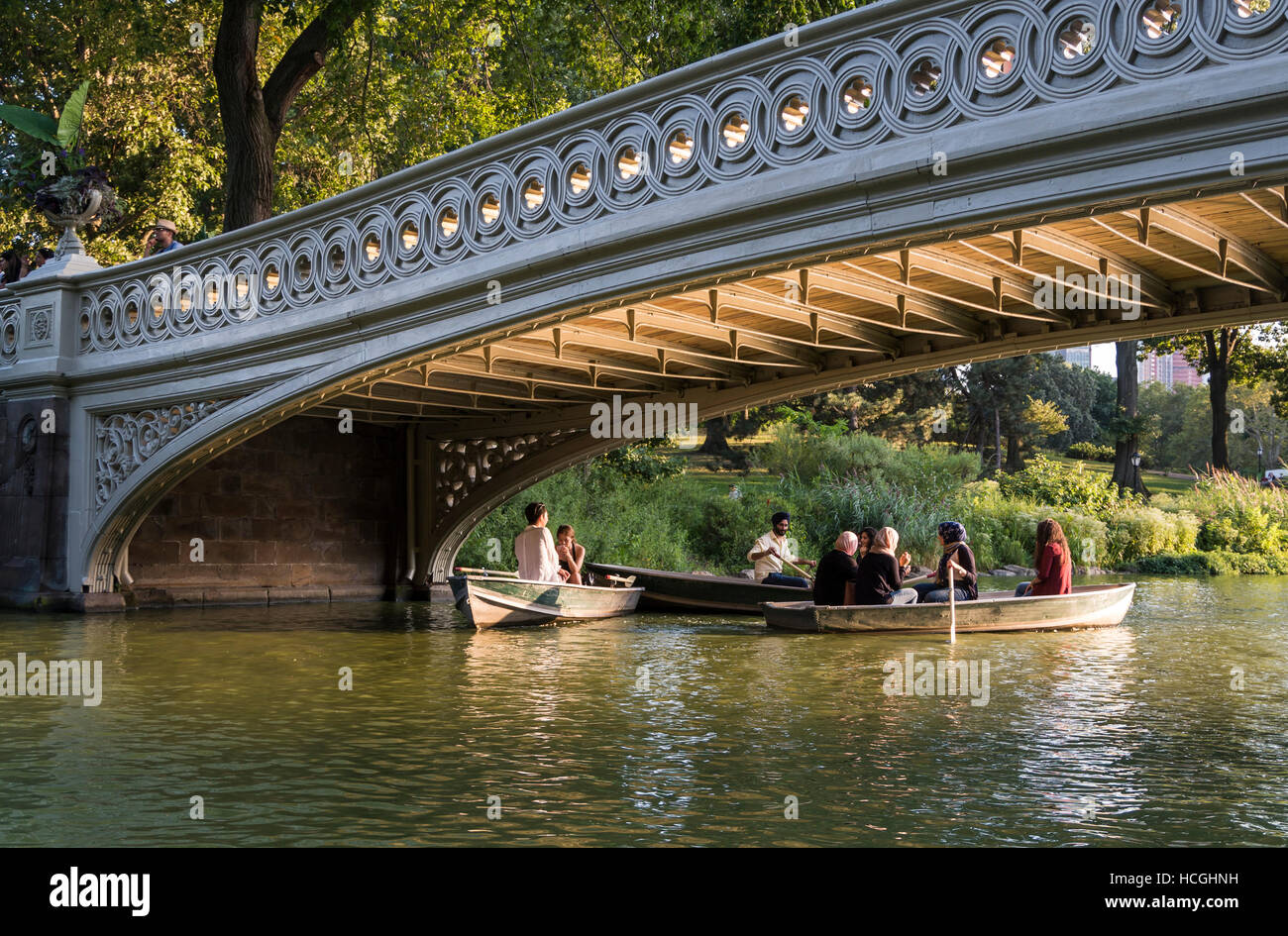 Menschen Bootfahren in Ruderboote im Sommer auf dem See unter Bogenbrücke im Central Park in New York City. Stockfoto